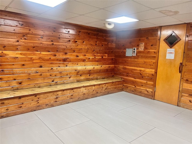 interior space featuring a drop ceiling, light tile patterned flooring, and wooden walls