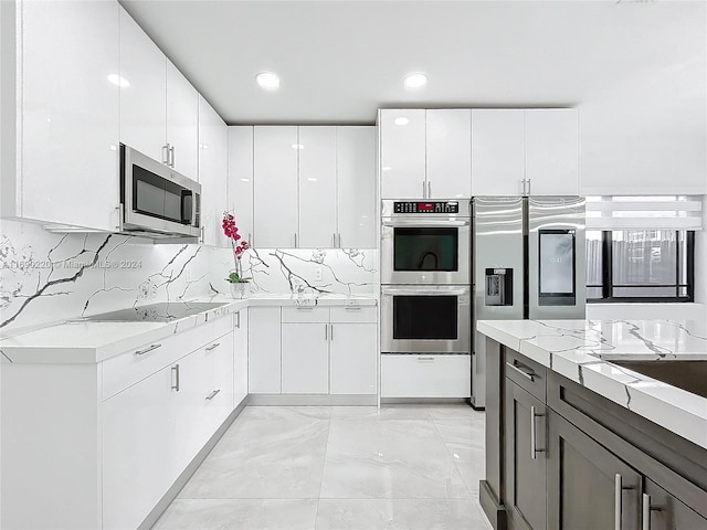 kitchen with white cabinets, appliances with stainless steel finishes, tasteful backsplash, and light stone counters