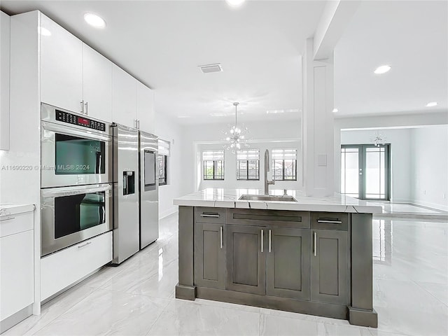 kitchen featuring stainless steel appliances, white cabinetry, sink, a kitchen island, and a notable chandelier