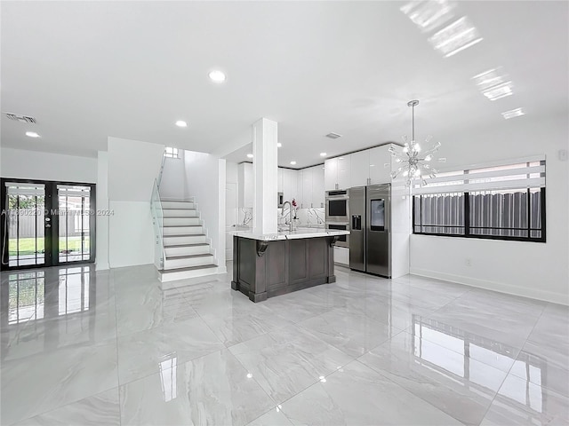 kitchen with stainless steel appliances, an island with sink, white cabinets, pendant lighting, and french doors