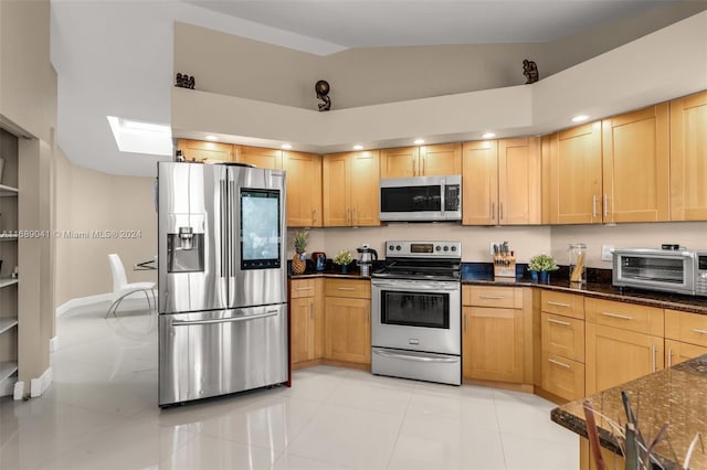 kitchen featuring stainless steel appliances, dark stone countertops, light tile patterned floors, and vaulted ceiling