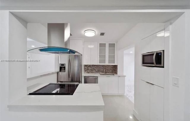 kitchen featuring island range hood, white cabinets, sink, backsplash, and appliances with stainless steel finishes