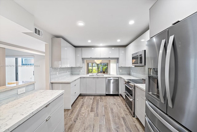 kitchen with decorative backsplash, light stone countertops, stainless steel appliances, white cabinets, and light hardwood / wood-style floors