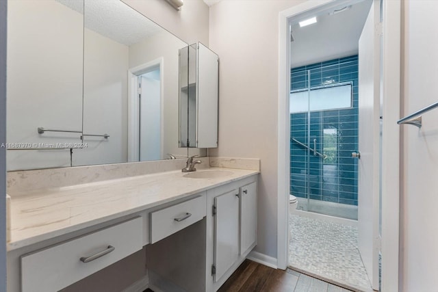 bathroom with wood-type flooring, vanity, a tile shower, and toilet