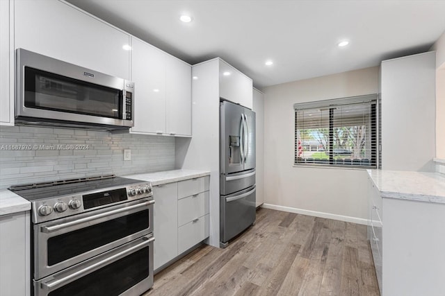 kitchen with light stone countertops, white cabinetry, light hardwood / wood-style floors, and appliances with stainless steel finishes