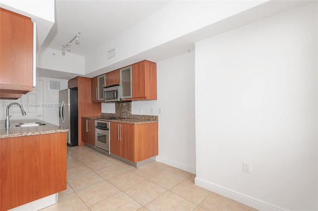 kitchen featuring sink, track lighting, appliances with stainless steel finishes, light tile patterned floors, and stone counters