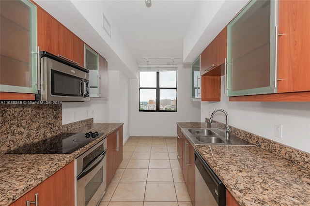 kitchen with track lighting, light tile patterned floors, sink, appliances with stainless steel finishes, and dark stone countertops