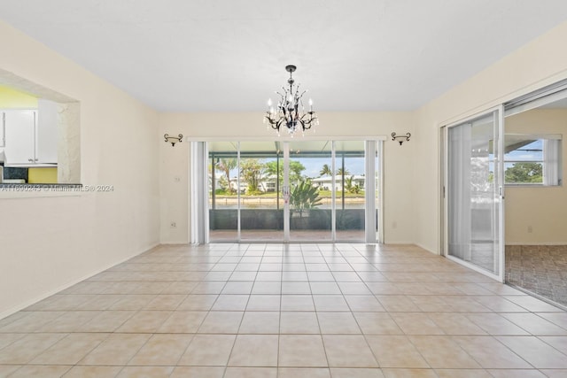 tiled empty room featuring a healthy amount of sunlight and an inviting chandelier