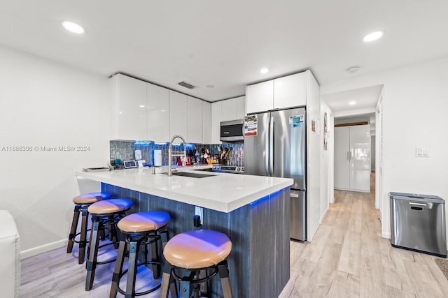 kitchen featuring kitchen peninsula, a kitchen breakfast bar, light wood-type flooring, stainless steel appliances, and white cabinetry