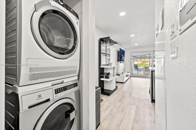 laundry area with light hardwood / wood-style floors and stacked washer / drying machine