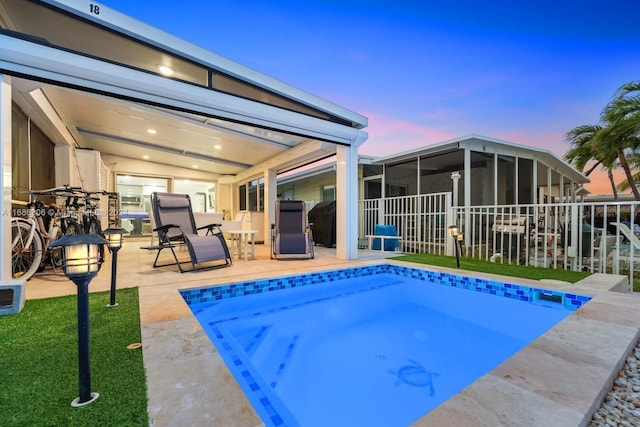 pool at dusk featuring a patio area and a sunroom