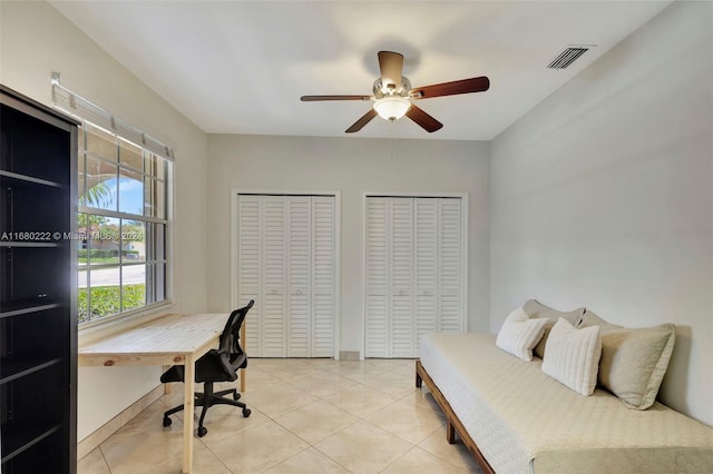 bedroom with light tile patterned flooring, ceiling fan, and two closets