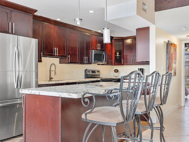 kitchen with hanging light fixtures, sink, light tile patterned flooring, light stone countertops, and appliances with stainless steel finishes