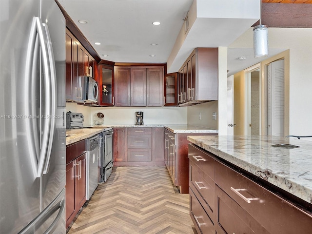 kitchen featuring light parquet floors, light stone countertops, pendant lighting, and appliances with stainless steel finishes