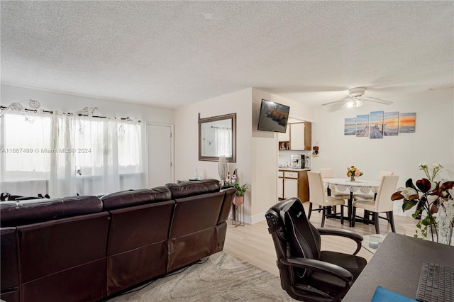 living room with ceiling fan, a textured ceiling, and light wood-type flooring