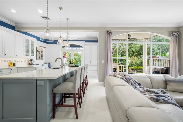 kitchen with sink, hanging light fixtures, a kitchen breakfast bar, an island with sink, and white cabinets