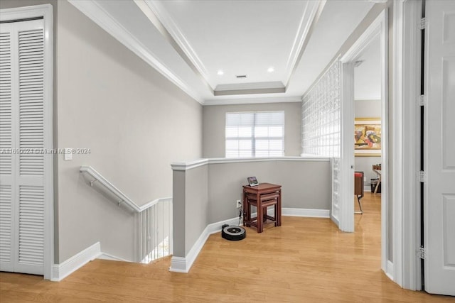 hallway featuring light wood-type flooring, a tray ceiling, and crown molding