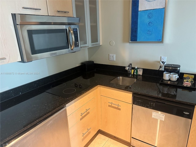 kitchen with appliances with stainless steel finishes, light tile patterned floors, light brown cabinetry, sink, and dark stone countertops