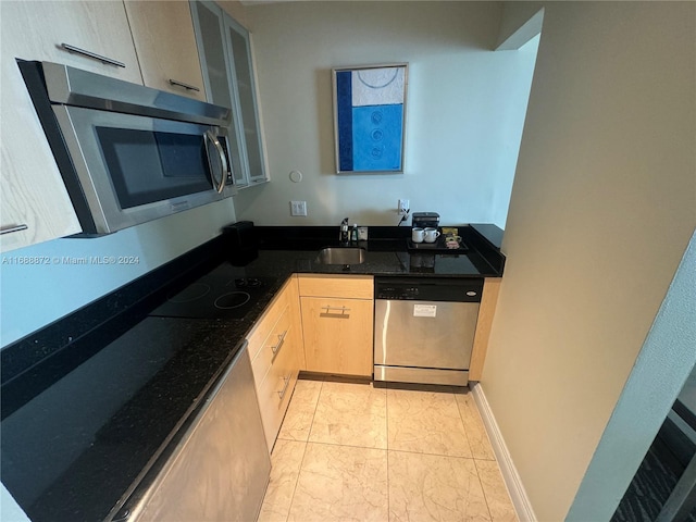 kitchen featuring stainless steel appliances, dark stone counters, light brown cabinetry, and sink