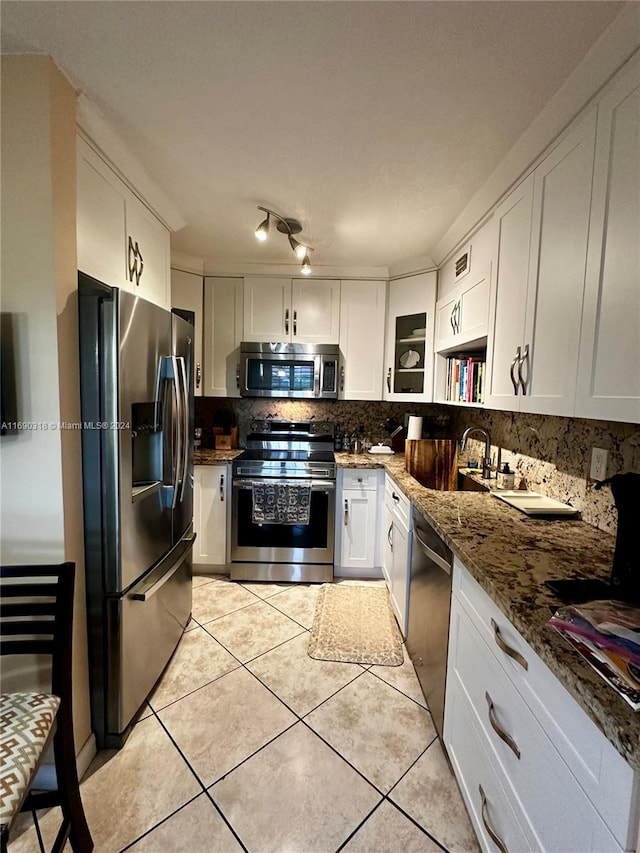 kitchen featuring stainless steel appliances, white cabinetry, sink, dark stone countertops, and light tile patterned floors