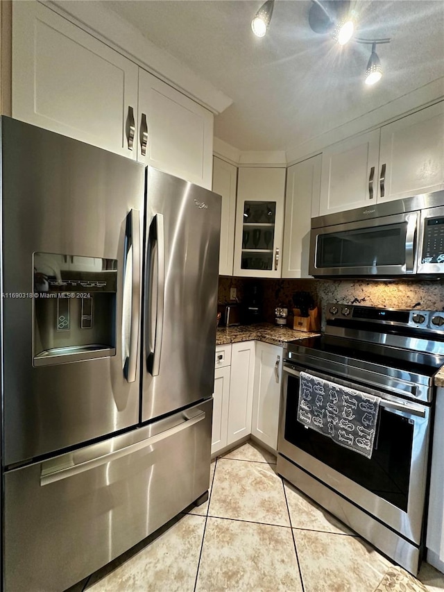 kitchen featuring white cabinetry, appliances with stainless steel finishes, dark stone counters, light tile patterned floors, and backsplash