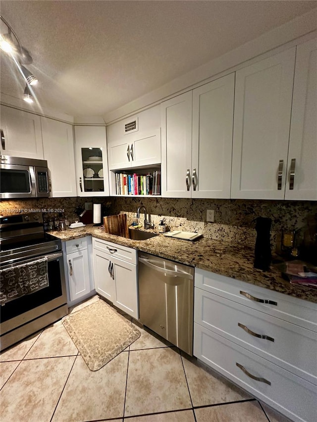 kitchen with stainless steel appliances, dark stone counters, a textured ceiling, light tile patterned floors, and white cabinets