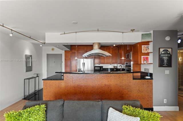 kitchen with stainless steel appliances, dark stone countertops, island range hood, hanging light fixtures, and light hardwood / wood-style flooring