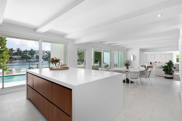 kitchen with beam ceiling, a center island, a water view, and light tile patterned floors