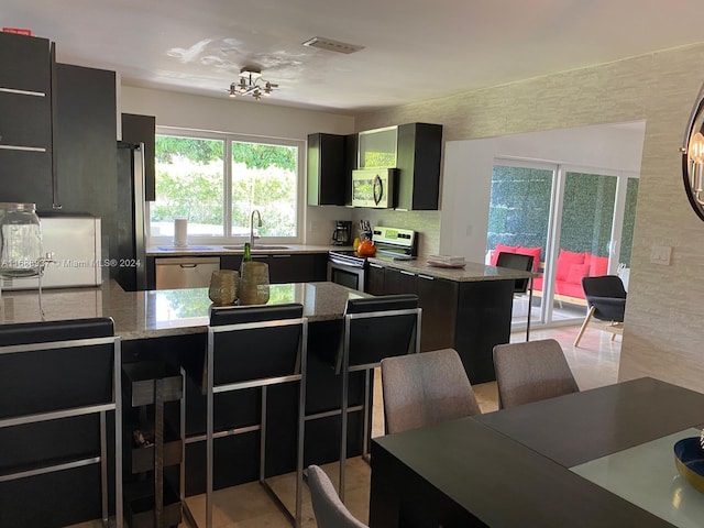 kitchen featuring stainless steel appliances, sink, a kitchen island, a breakfast bar, and light stone countertops