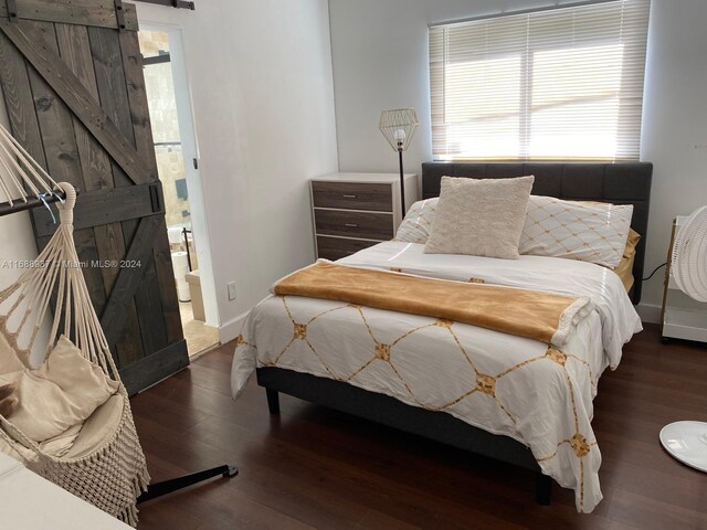 bedroom featuring dark hardwood / wood-style flooring, a barn door, and connected bathroom