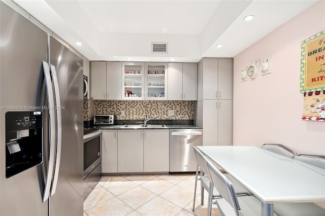 kitchen featuring sink, appliances with stainless steel finishes, light tile patterned floors, backsplash, and gray cabinetry