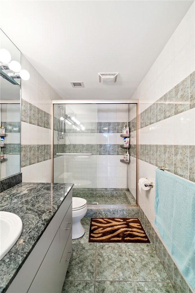 bathroom with toilet, a shower with door, tile walls, tile patterned flooring, and vanity