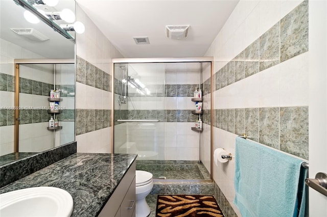 bathroom with a shower with shower door, vanity, toilet, and tile walls