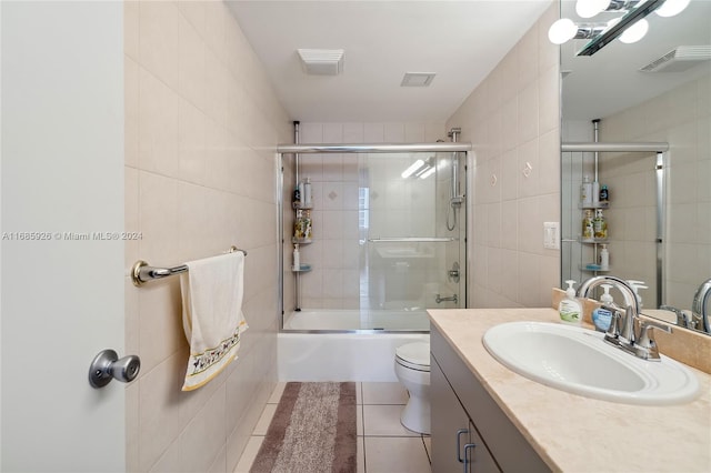 full bathroom with tile walls, tile patterned floors, vanity, bath / shower combo with glass door, and toilet