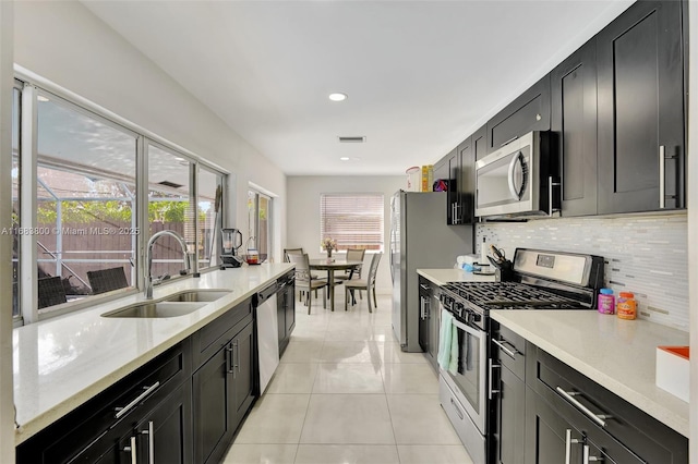 kitchen featuring sink, light stone countertops, appliances with stainless steel finishes, tasteful backsplash, and light tile patterned flooring