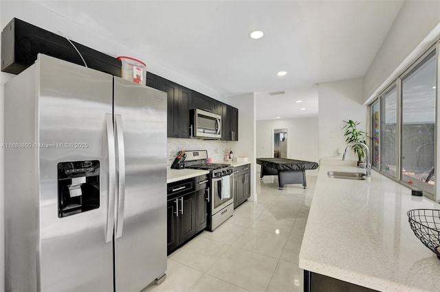 kitchen featuring light stone countertops, sink, stainless steel appliances, backsplash, and light tile patterned floors