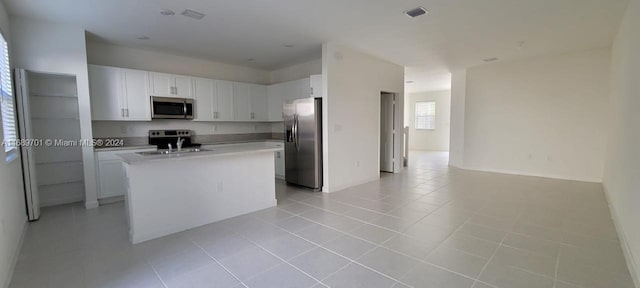 kitchen featuring stainless steel appliances, light tile patterned flooring, white cabinetry, sink, and an island with sink