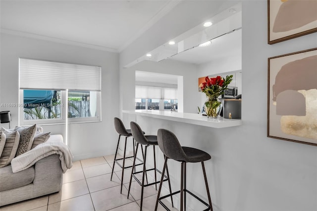 kitchen with a kitchen bar, kitchen peninsula, light tile patterned floors, and ornamental molding