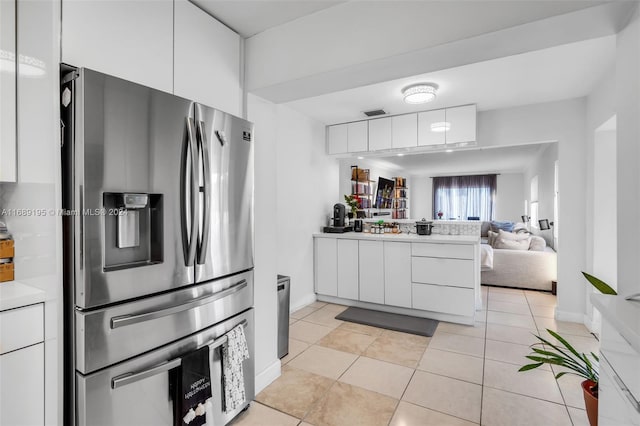 kitchen with kitchen peninsula, light tile patterned floors, stainless steel refrigerator with ice dispenser, and white cabinetry