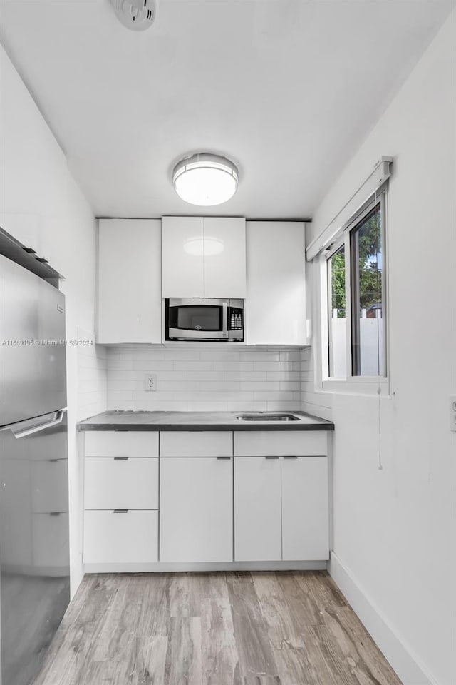 kitchen featuring white cabinets, backsplash, appliances with stainless steel finishes, and light hardwood / wood-style floors