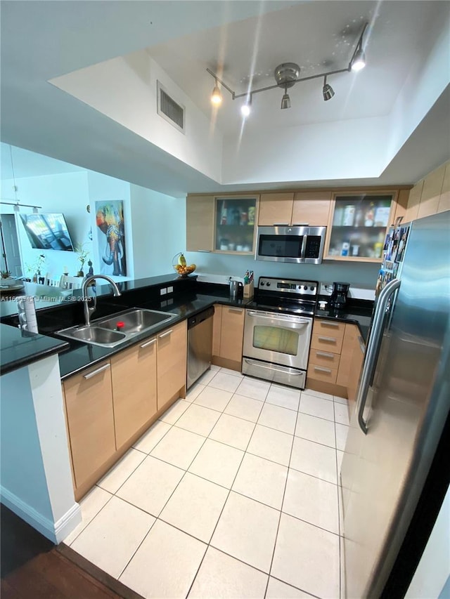 kitchen with appliances with stainless steel finishes, track lighting, a raised ceiling, sink, and light tile patterned flooring