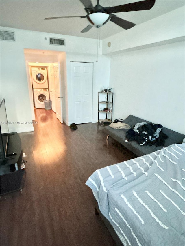 bedroom with hardwood / wood-style floors, ceiling fan, and stacked washer and clothes dryer