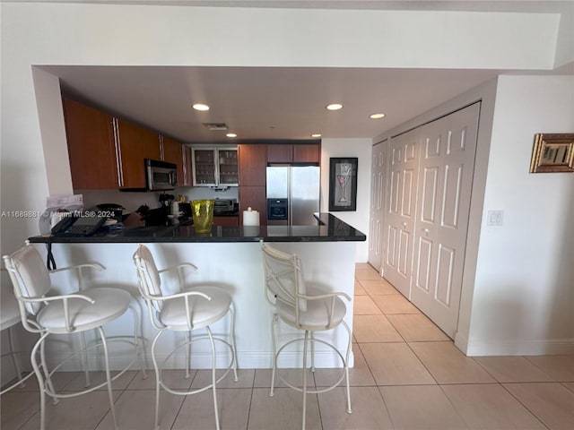 kitchen with kitchen peninsula, stainless steel appliances, a breakfast bar area, and light tile patterned flooring