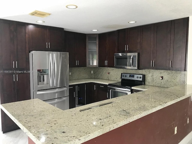 kitchen with stainless steel appliances, light stone counters, kitchen peninsula, and tasteful backsplash