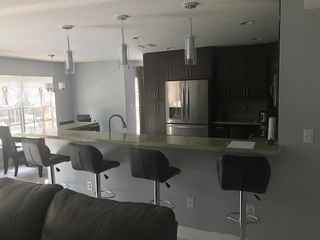 kitchen with light stone counters, stainless steel fridge, decorative light fixtures, a breakfast bar, and kitchen peninsula