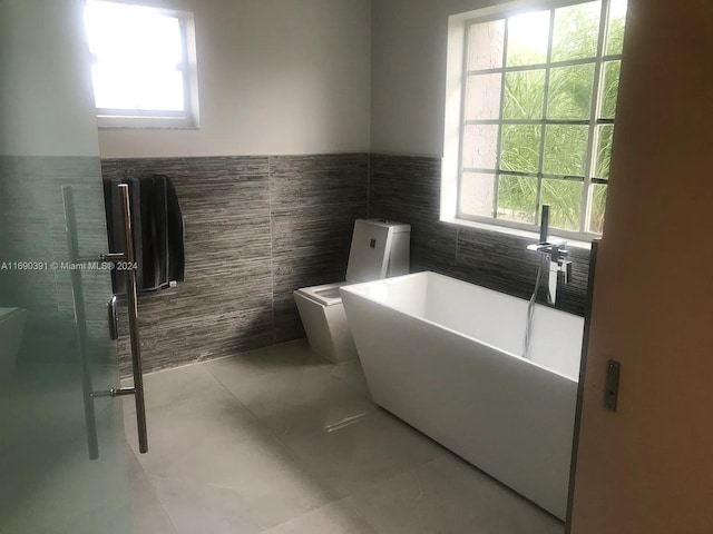 bathroom featuring toilet, tile walls, a tub, and a healthy amount of sunlight