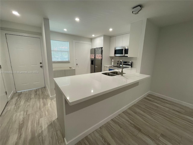 kitchen featuring white cabinetry, kitchen peninsula, light hardwood / wood-style floors, and stainless steel appliances