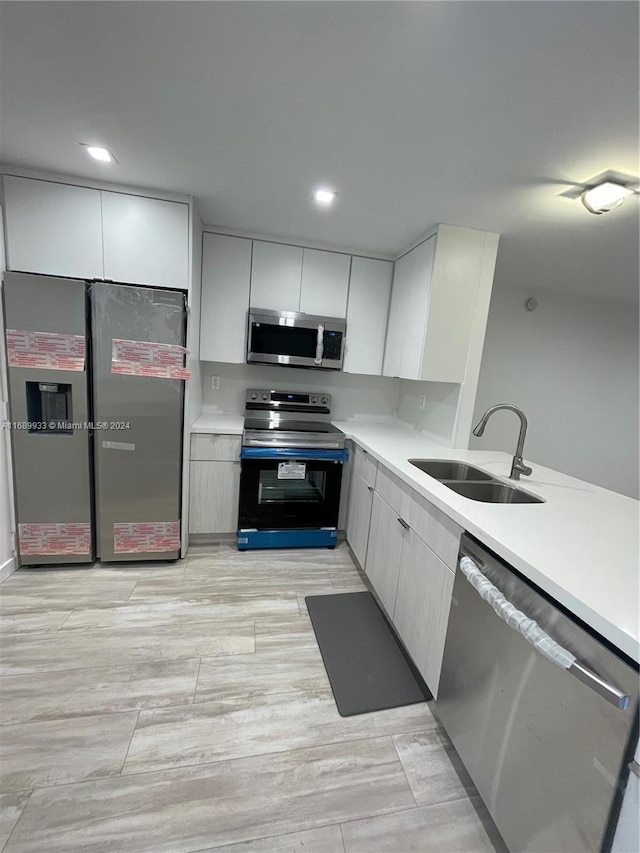 kitchen with light wood-type flooring, appliances with stainless steel finishes, sink, and white cabinets