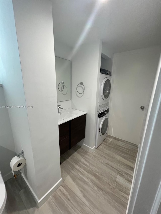 laundry room with light hardwood / wood-style floors, stacked washer and clothes dryer, and sink