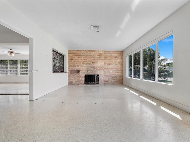 unfurnished living room featuring ceiling fan, a stone fireplace, and brick wall